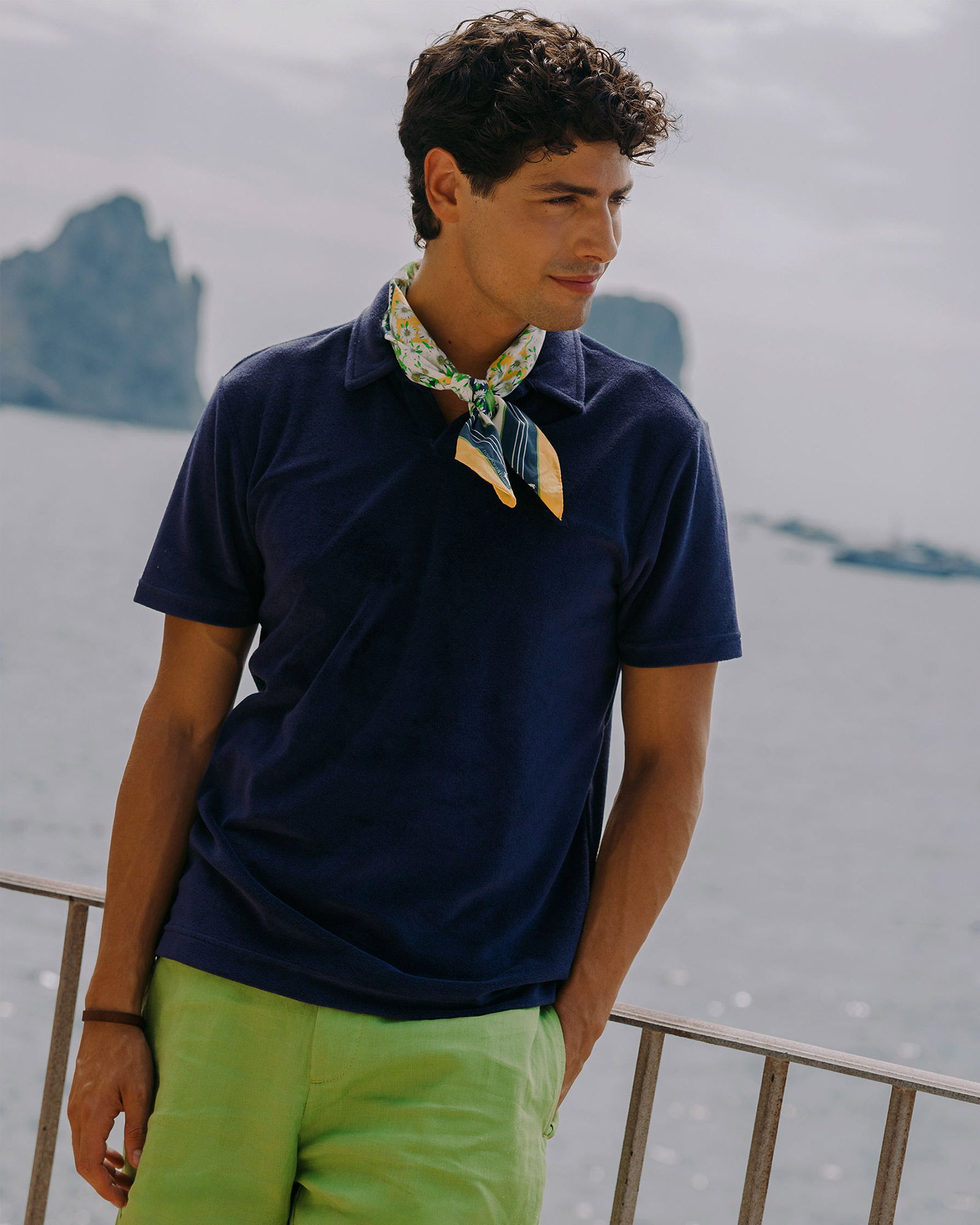 Man in navy polo and green shorts by the sea